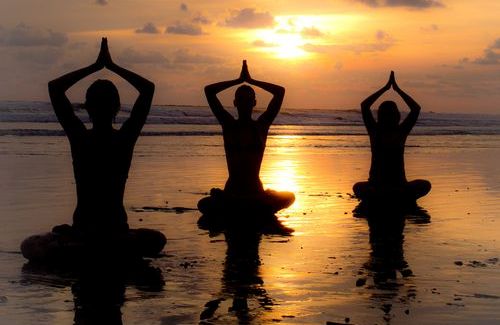 Tre mennesker gjør yoga på en strand