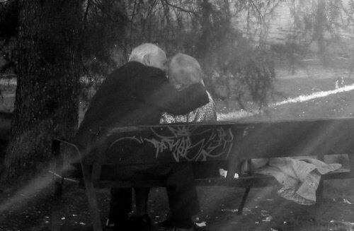 Eldre par kysser på en benk