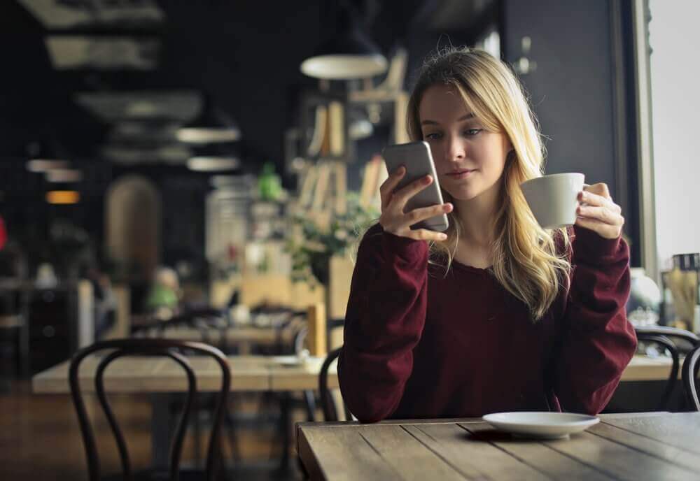 Kvinne på kafé er avhengig av mobiltelefonen sin