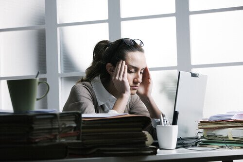 Kvinne med stresshodepine foran en datamaskin på jobben