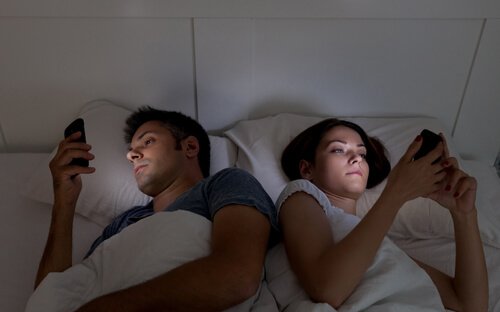 Par i sengen på hver sin telefon