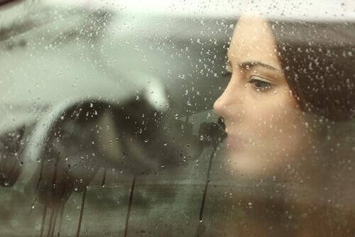 Trist kvinne bak vindu med regn