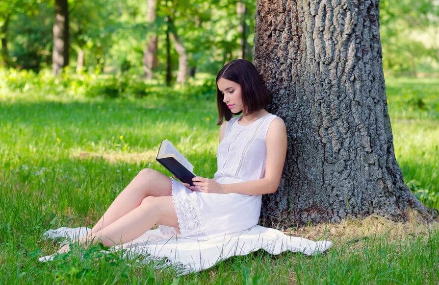 Kvinne leser bok under et tre
