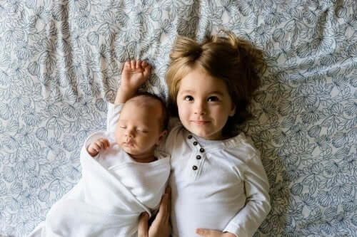En baby og en liten gutt som ligger i sengen.