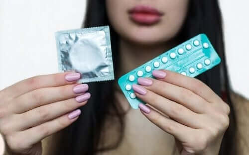 Kvinne holder opp en kondompakke og en pakke med p-piller