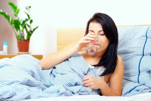 En kvinne som drikker vann i sengen.