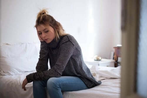 En kvinne med hodepine som sitter på sengen