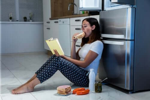 Kvinne sitter foran kjøleskapet og spiser