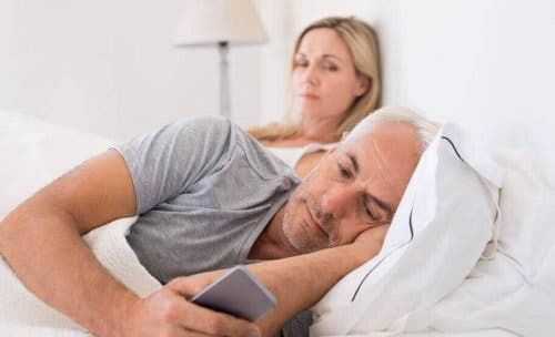 En mann på mobilen i sengen med kjæresten ved siden av seg