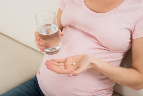 En gravid kvinne med en pille og et glass vann