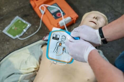 En som bruker defibrillator på en øvelsesdukke for hjertestans.