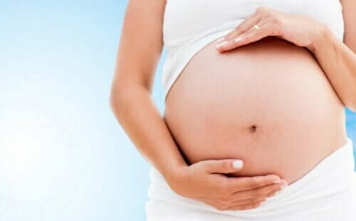 En gravid kvinne i hvitt, som holder seg på magen, en av kontraindikasjonene for merian er bruk under graviditet