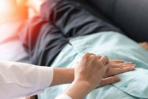 Tykktarmskreftpasient som legger seg på sofaen med legens hender på torso