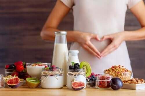 Kvinne som lager hjerte med hendene over magen bak mat som yoghurt, frukt og nøtter