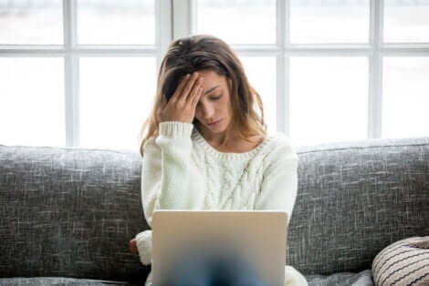En kvinne som opplever stress mens hun jobber på den bærbare datamaskinen på sofaen.