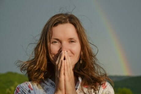En kvinne som ber foran en regnbue.