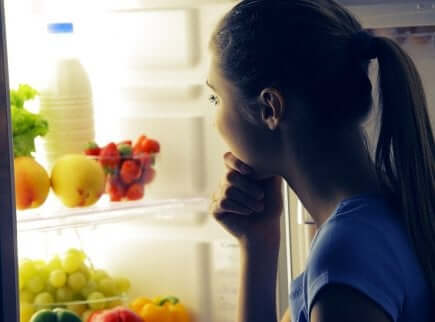 En kvinne som ser på frukt og melk i kjøleskapet om natten.