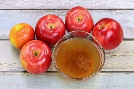 Epler som ligger rundt et glass med eplecidereddik