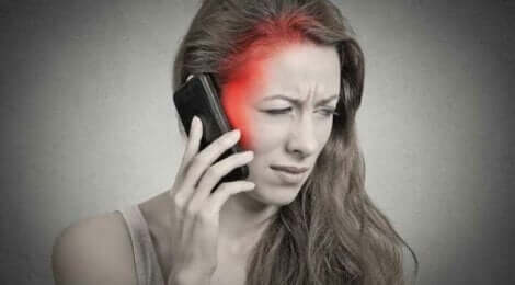 En kvinne med hodepine som holder mobilen