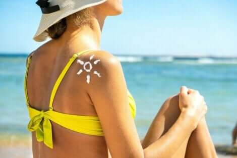 En kvinne som sitter på stranden med en sol laget av solkrem på skulderen.