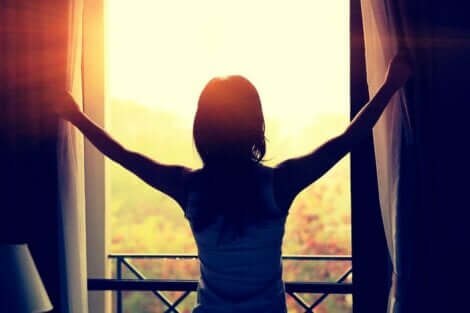 En kvinne som åpner gardinene på en solskinnsdag.