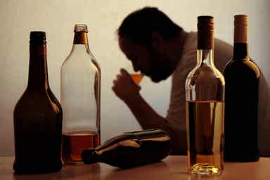 En mann som drikker et glass alkohol, omgitt av forskjellige flasker