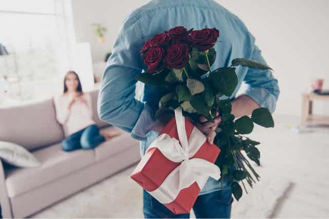 En mann som overrasker partneren med blomster og en gave