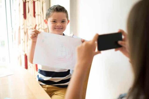 En gutt med downs syndrom som holder en tegning mens moren tar et bilde.