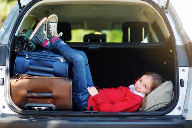 Et barn som hviler bak på en parkert bil med bena på koffertene