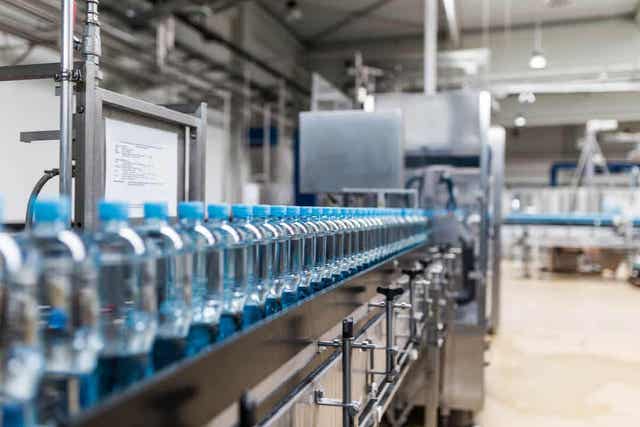 Vannflasker i plast som beveger seg nedover en fabrikklinje.