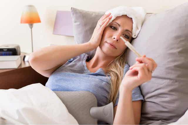 En kvinne som ligger i sengen med feber og tar temperaturen