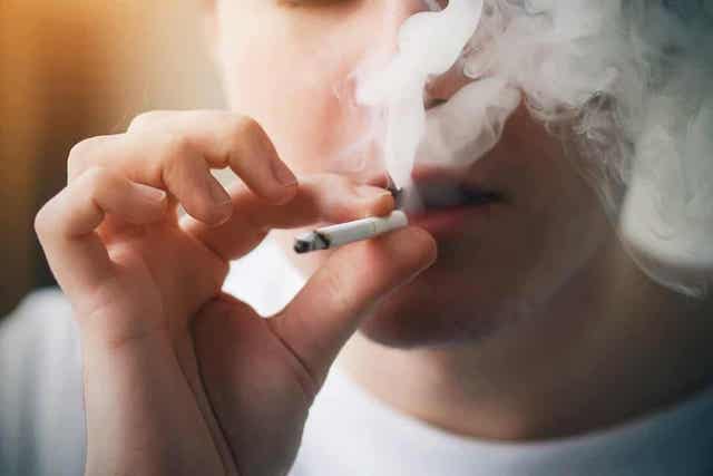 En ung mann som puster ut sigarettrøyk