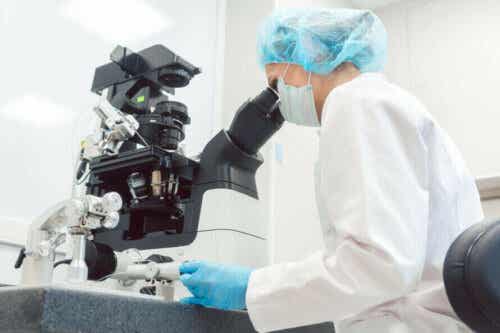 En laboratorietekniker som ser inn i et mikroskop.