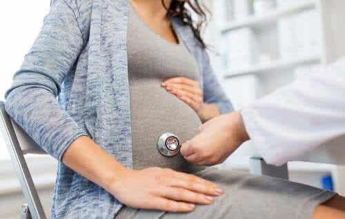 En lege legger et steteskop på en gravid kvinnes mage.