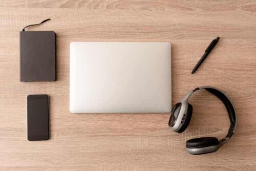 En planlegger, en smarttelefon, en bærbar datamaskin, en penn og hodetelefoner pent arrangert på et skrivebord.