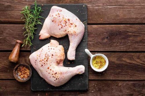 Rå kylling på et skjærebrett med olivenolje, krydder og urter.