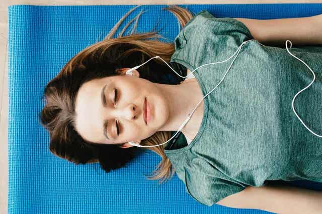En kvinne som ligger på en matte med lukkede øyne og lyttet til hodetelefoner.